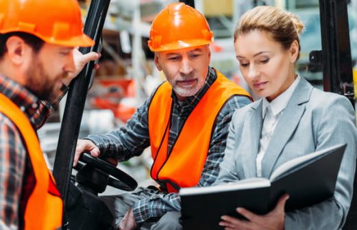 two workers and inspector using forklift machine in storehouse